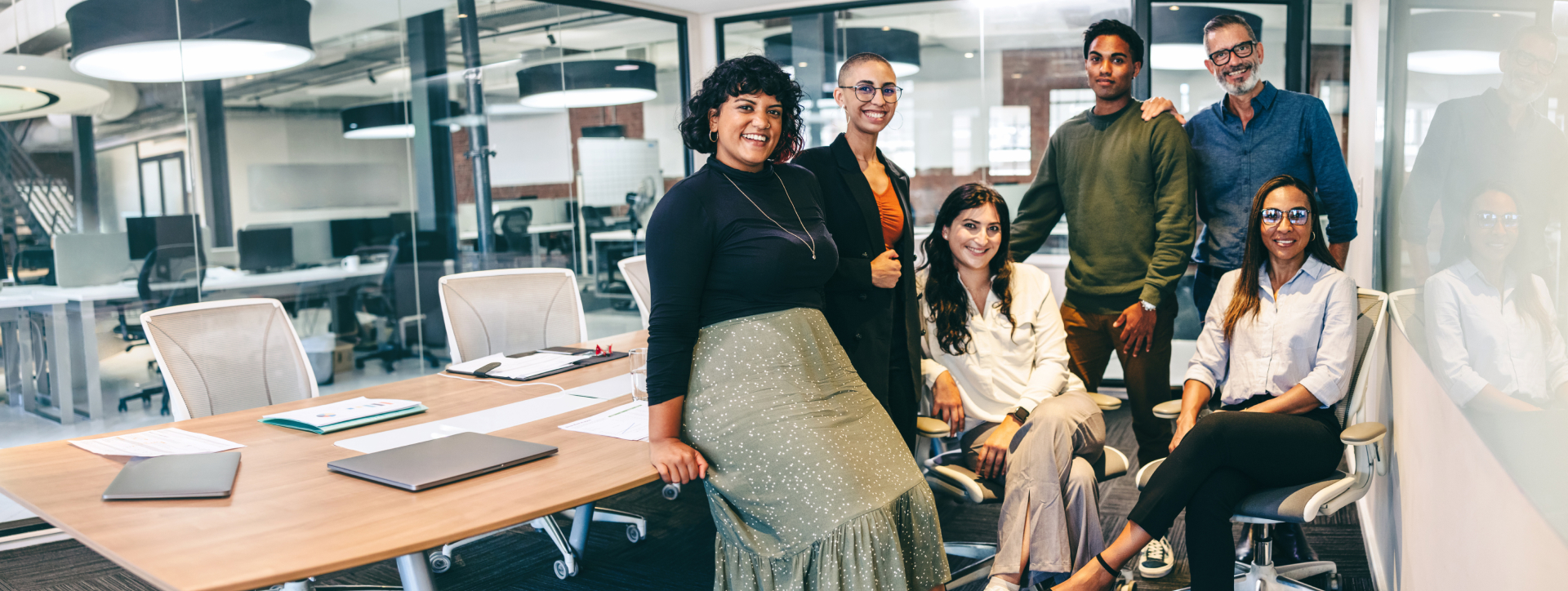 A diverse group of people sat down and standing up smiling in a meeting room.