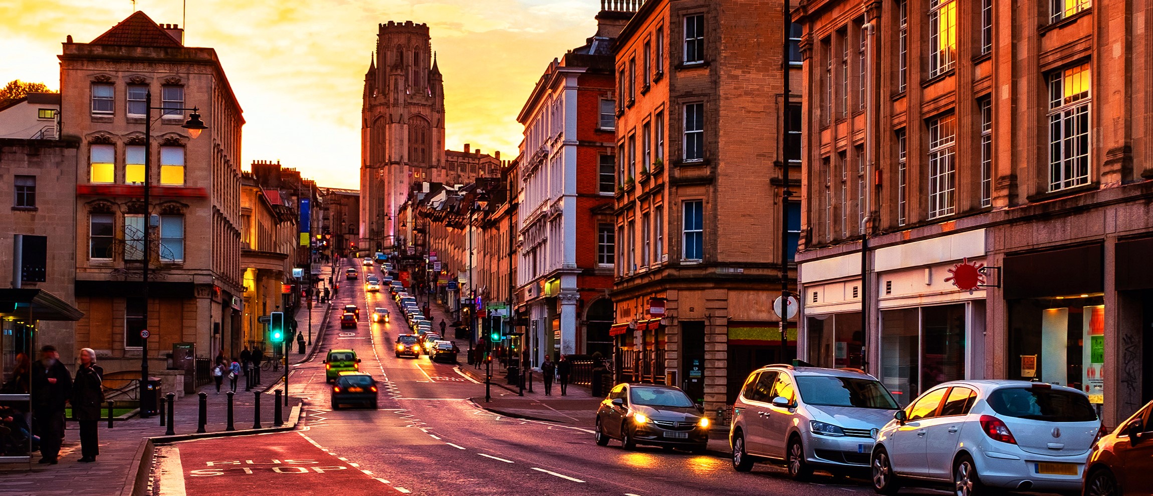 A steep road in the city centre being lit orange from the sun set.