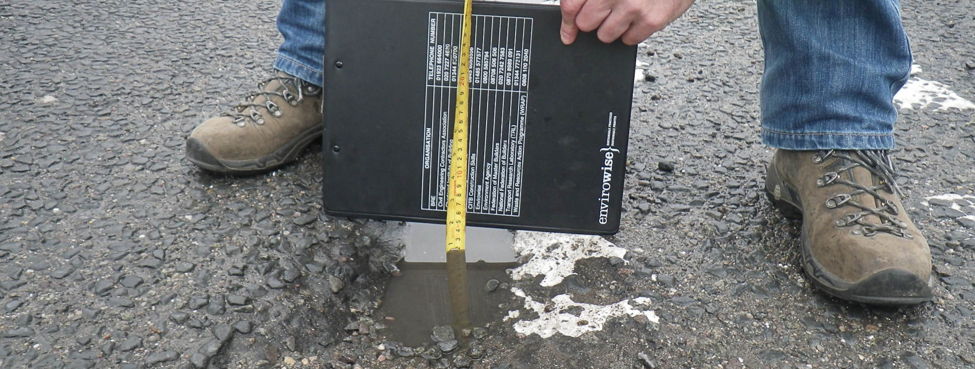 A man carrying out a road safety audit where he is measuring a pothole.