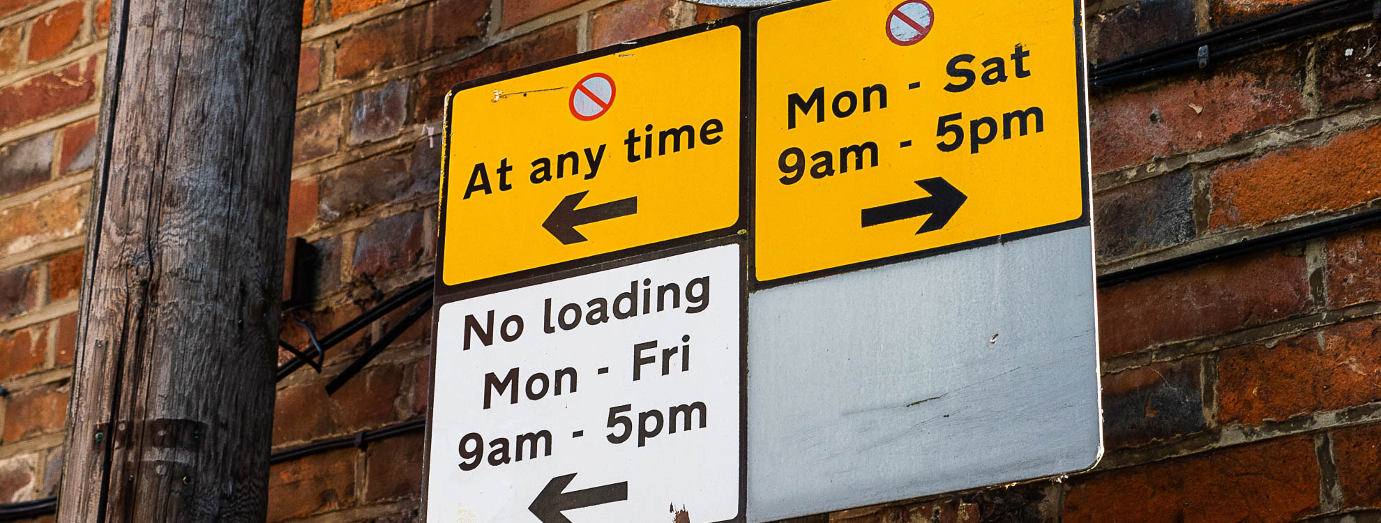 Various parking restriction signs attached to a metal pole in front of a brick wall.