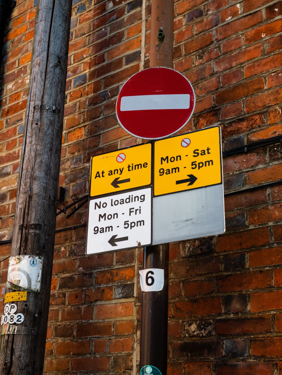 Various parking restriction signs attached to a metal pole in front of a brick wall.